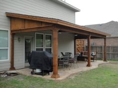 an outdoor covered patio with grill and table in the back yard next to a house