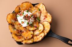 a skillet filled with potato wedges topped with sour cream and bacon on top