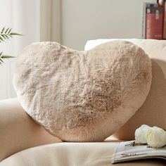 a heart shaped pillow sitting on top of a couch next to a book and flower