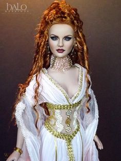 a doll with red hair wearing a white dress and gold jewelry on it's head