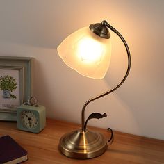 a desk lamp on top of a wooden table next to a clock and framed photograph