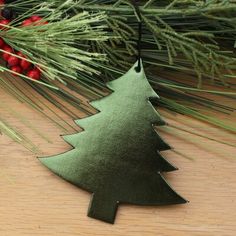 a metal christmas tree ornament hanging from a pine branch on a wooden table