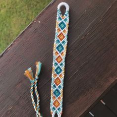 a blue, orange and yellow beaded lanyard with tassels sitting on top of a wooden table