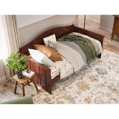 a bed sitting on top of a wooden floor next to a table with a potted plant