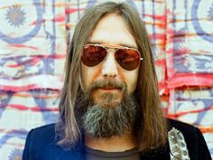 a man with long hair and sunglasses standing in front of a wall