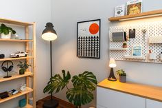 a room with shelves, plants and pictures on the wall above it is also a lamp