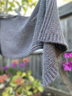 a gray sweater hanging from a clothes line in front of potted plants and flowers