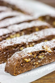 some brownies are on a white plate with powdered sugar and walnut toppings