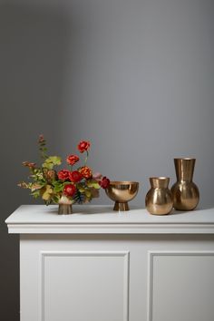 vases and bowls on top of a white cabinet with red flowers in the middle