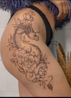 a woman's thigh with flowers and a dragon tattoo on it, next to a wall