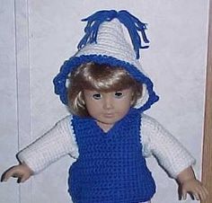 a doll wearing a crocheted hat and blue dress is standing in front of a door