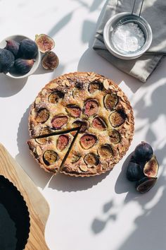 a pie sitting on top of a white table next to figs and other food