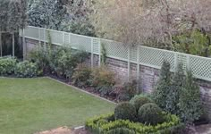 a garden with green grass and bushes next to a brick wall that has a trellis on it