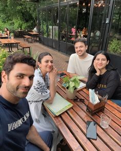 four people sitting at a wooden table outside