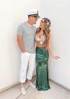 a man standing next to a woman in a green mermaid skirt and white sailor hat