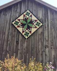 a wooden building with a quilt hanging on it's side and flowers in the foreground