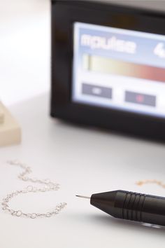 a pen sitting on top of a white table next to a computer monitor and chain