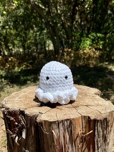 a crocheted white object sitting on top of a tree stump in the woods