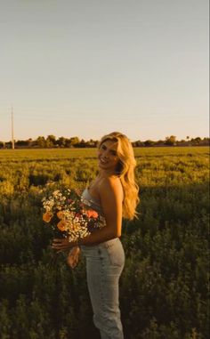 a woman standing in the middle of a field with flowers on her hand and smiling at the camera