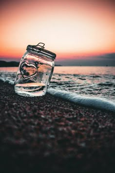 a jar filled with water sitting on top of a beach next to the ocean at sunset