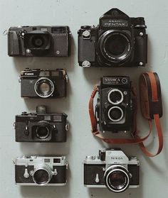 several different cameras sitting next to each other on a wall with leather straps around them