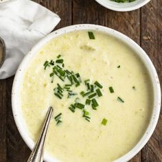 two bowls filled with soup on top of a wooden table next to silver spoons