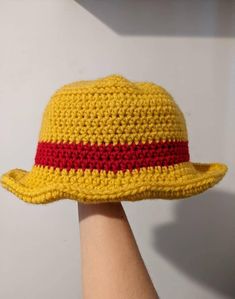 a crocheted yellow hat with red stripes on the brim is held up by a person's hand