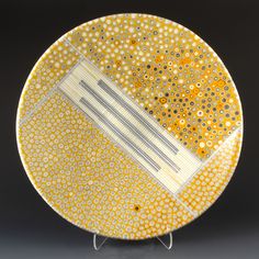 a yellow and white plate sitting on top of a metal stand next to a black wall