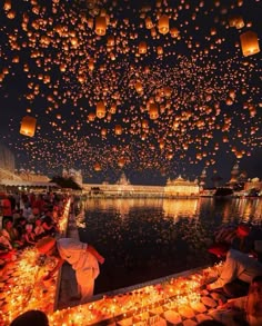 many people are flying lanterns over the water