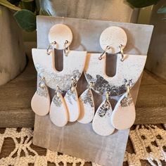 four pairs of white and silver earrings are on display in front of a potted plant