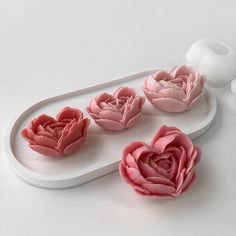 three pink flowers sitting on top of a white tray