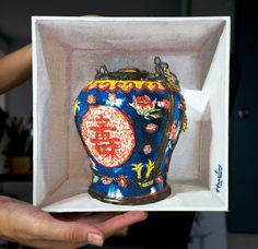 a hand holding up a blue and red vase in a white box with writing on it