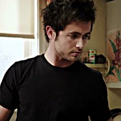 a man standing in a kitchen looking down at something on the counter and wearing a black t - shirt