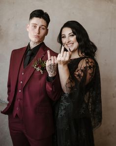 a man in a red suit standing next to a woman wearing a black lace dress