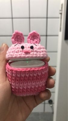 a hand holding a pink knitted cup holder in the shape of a mouse with ears