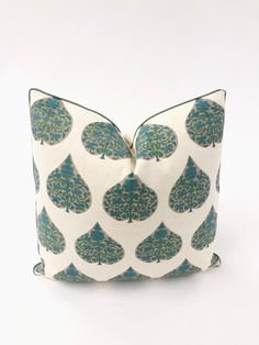 a white pillow with blue and green designs on the front, sitting against a white background