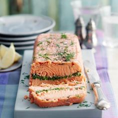 a large piece of salmon on a plate with some lemon wedges and water in the background