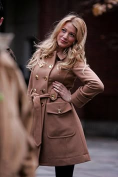 a woman in a trench coat standing on the street with her hands on her hips