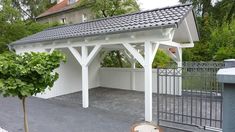 a white gazebo with a black roof and some bushes in front of the fence