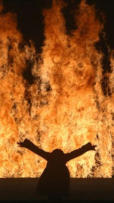 a person standing in front of a large fire with their arms spread out and hands outstretched