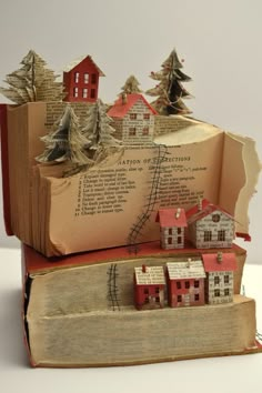 an open book with houses on it and trees in the pages, sitting on top of each other