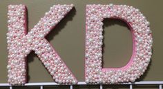 the letters k and d are made out of pink pearls on a white wire rack