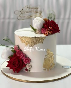 a white and gold cake with red flowers on top