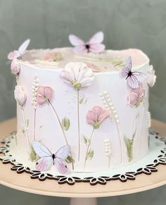 a white cake with pink flowers and butterflies on it sitting on a table next to a wall