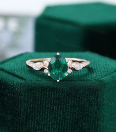 an emerald and diamond ring sitting on top of a green velvet box