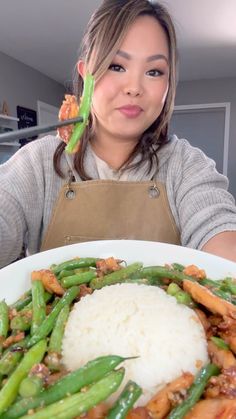 a woman is holding a plate with green beans and rice on it while looking at the camera