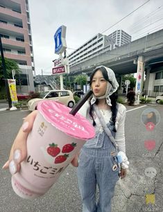 a woman holding an ice cream cup in front of her face while standing on the street