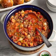 a blue bowl filled with meat and vegetables next to bowls of bread on the side