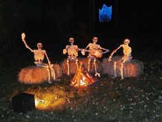 three skeletons sitting on hay bales around a campfire in the grass at night