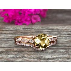 a yellow and white diamond ring on top of a wooden table next to pink flowers